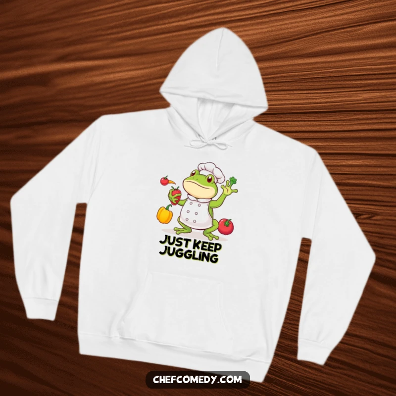Funny frog chef character in a dynamic pose, juggling vibrant vegetables, wearing a chef hat, on a cozy hoodie.